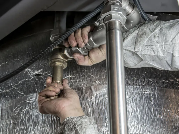 Plumber tightening a pipe fitting under a sink