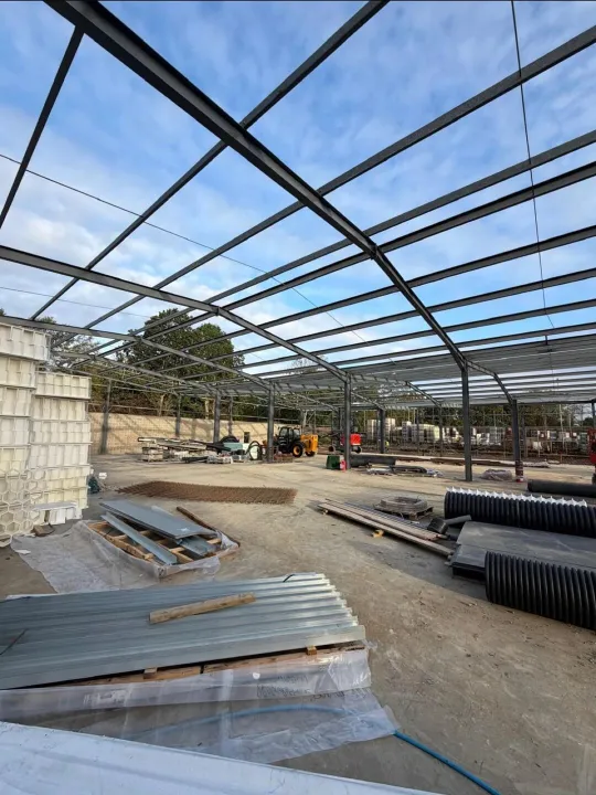 Dark painted steel portal frame with stacked roof sheets and drainage pipe on the site slab