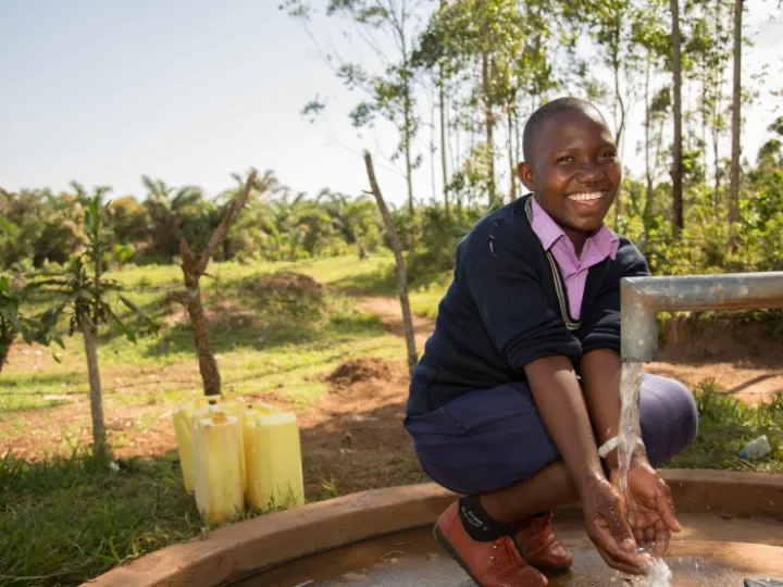 Prossy Nabiryo chair of St Balikddembe schools health club (SHC) using a new community water pump &ndash; Copyright All We Can