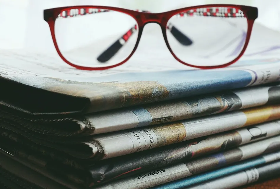 Red eyeglasses resting on a stack of newspapers symbolize reading and information.