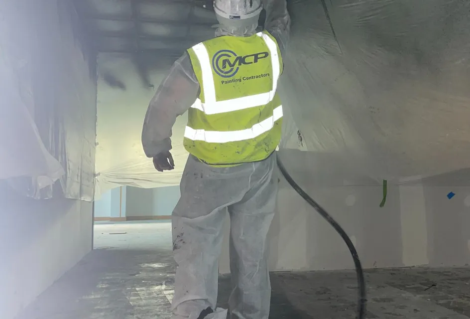 Construction worker wearing hi-vis jacket spraying surface