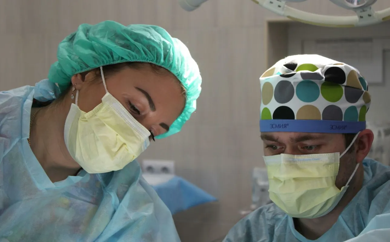 Surgeons wearing masks and scrubs conduct an operation in a hospital setting.
