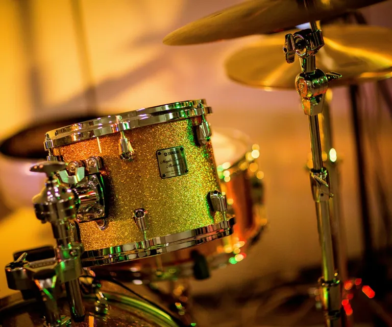 A vibrant close-up photo of a glittery drum set under concert lights, evoking a lively music performance.