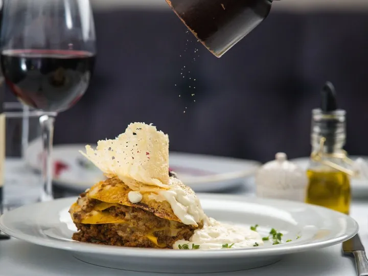 A layered pasta dish with a parmesan crisp, served with red wine