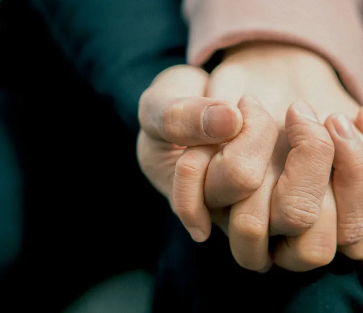 A close-up photo capturing two adult hands holding each other, symbolizing love and support.
