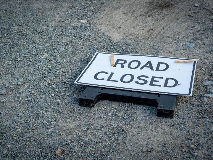 A road closed sign lies on a gravel pathway