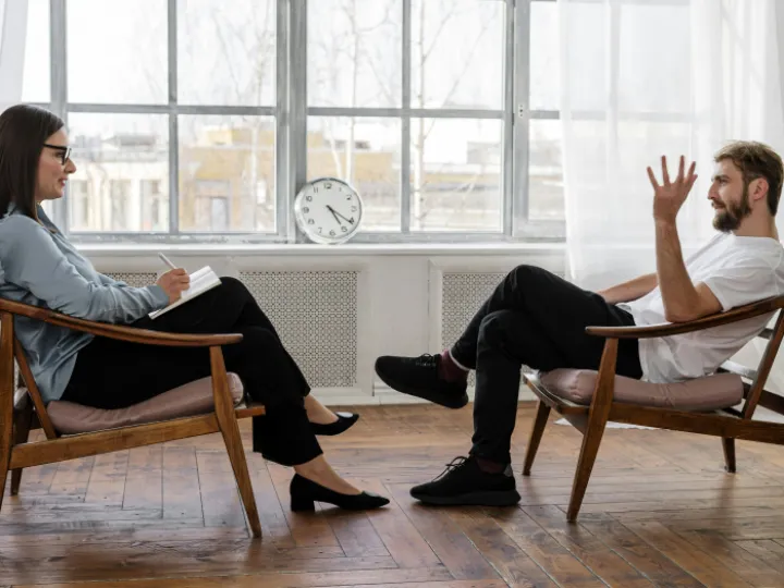 Person in Black Pants and Black Shoes Sitting on Brown Wooden Chair