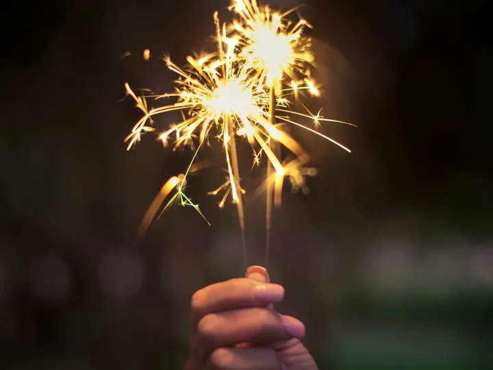 A hand holding sparklers glowing brightly in a dark night, capturing the essence of celebration.