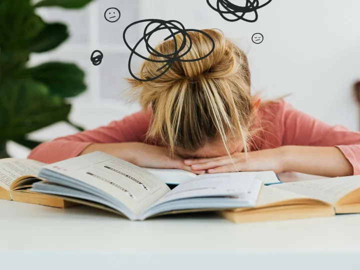 Young woman asleep over books at desk, conveying stress and mental overload.