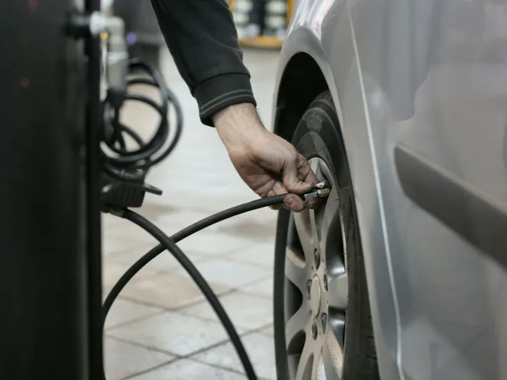 Mechanic inflating a car tire inside an auto repair shop, ensuring optimal tire pressure.