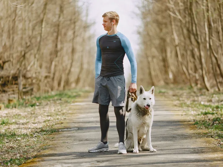A young man in sportswear enjoying a leisurely walk with his white shepherd dog on a forest path.