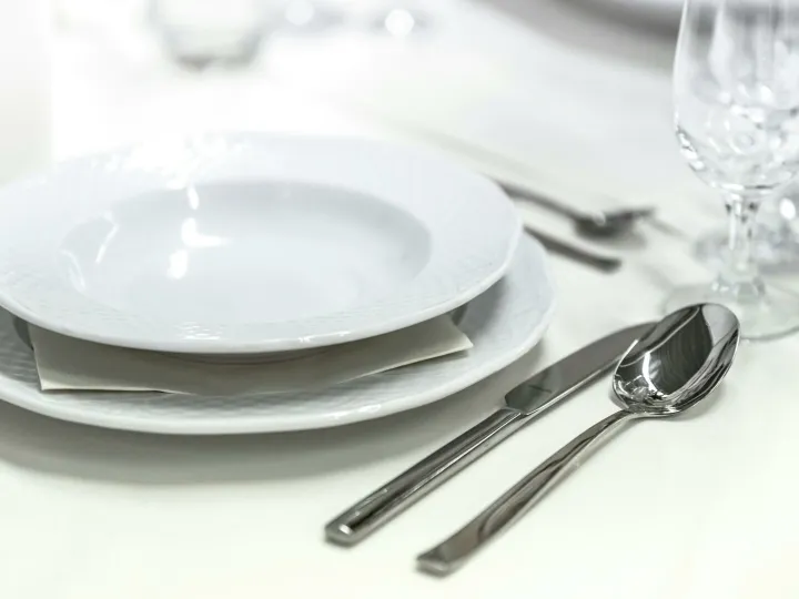 Elegant dining table with white porcelain plates and silver cutlery elegantly arranged.