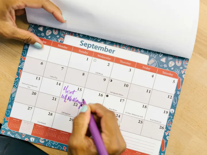 A person marking a calendar in September with a purple pen on a wooden desk.