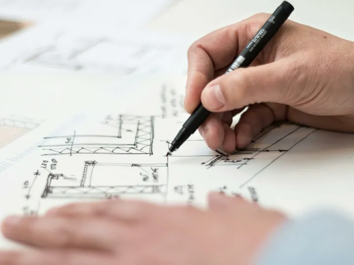 Close-up of hand drawing intricate technical designs on blueprint with pen, ideal for engineering or architecture themes.