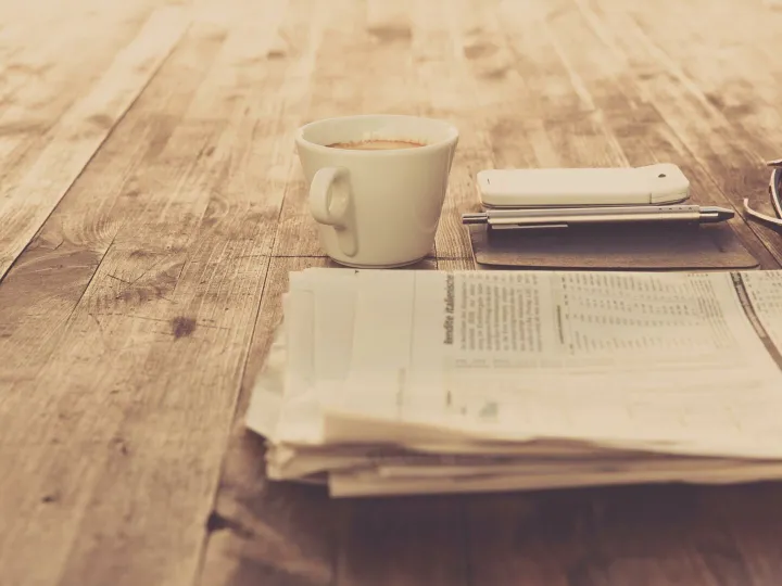 A warm vintage morning setup with coffee, newspaper, and smartphone on wooden table.
