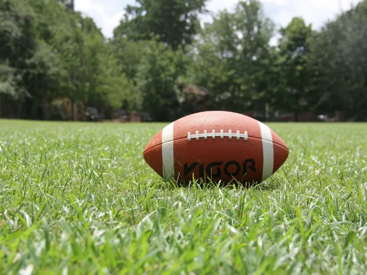 A close-up of an American football on a grassy field, highlighting outdoor sports in summer.