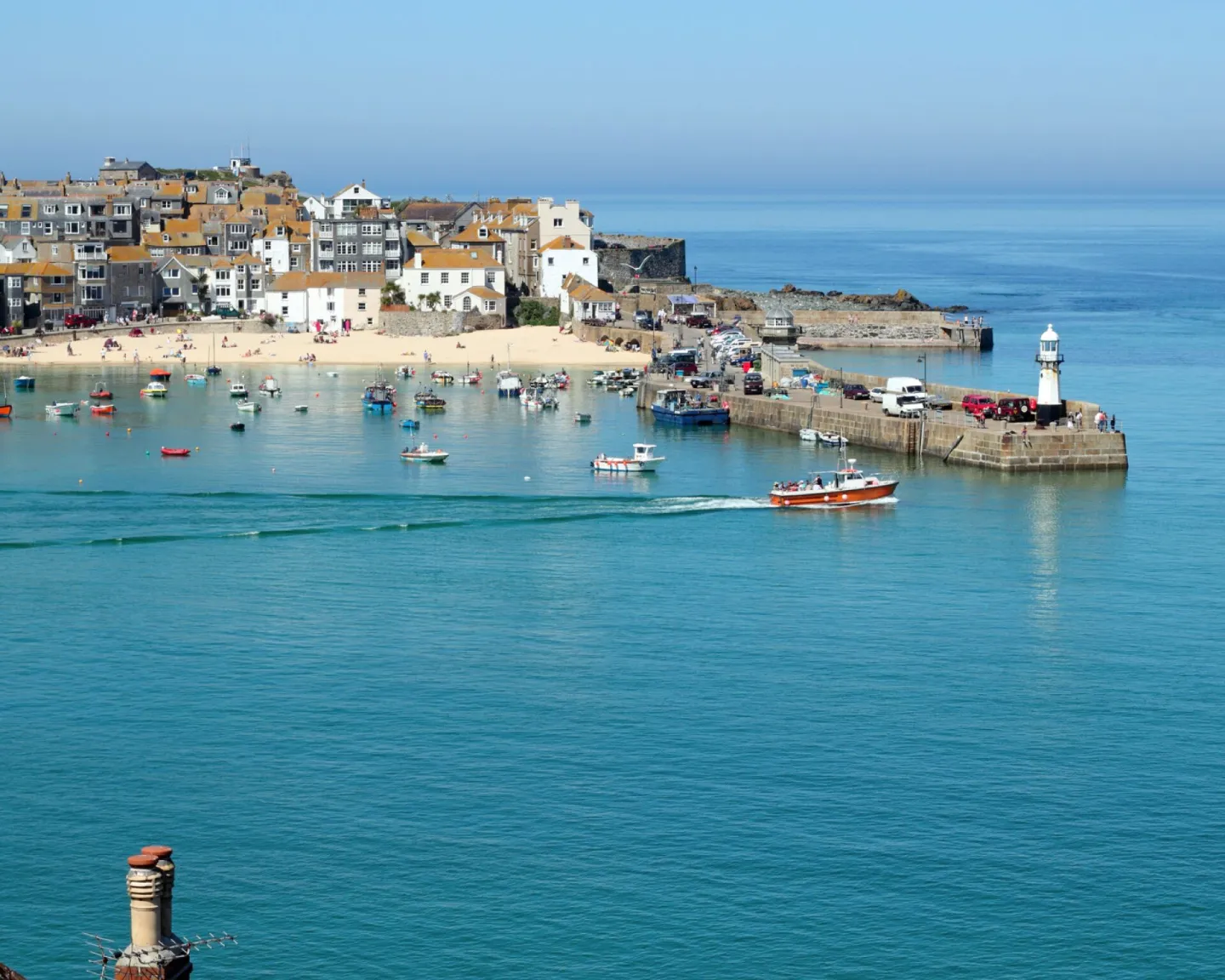 A Cornish harbour with fishing boats, a lighthouse and a sandy beach