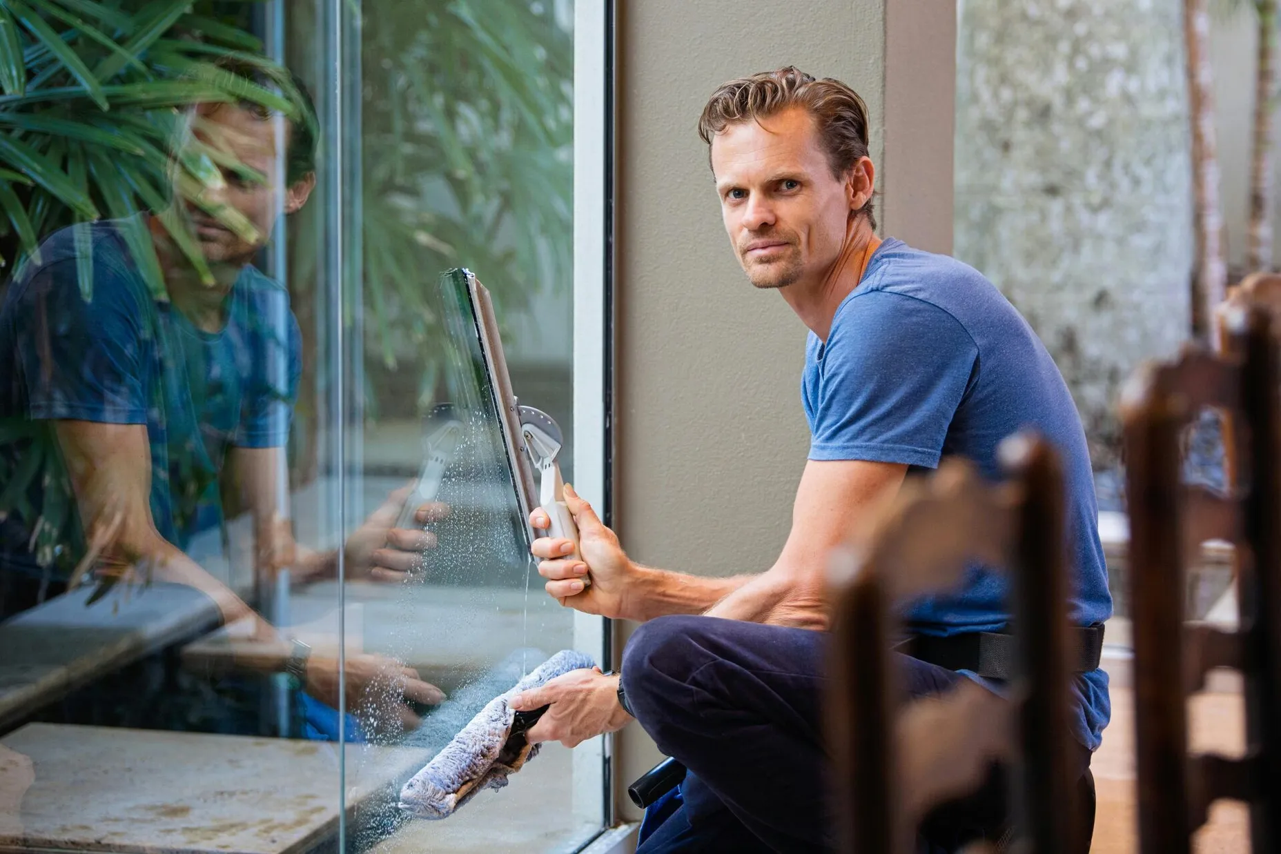 A man in a blue t-shirt cleaning large glass pane