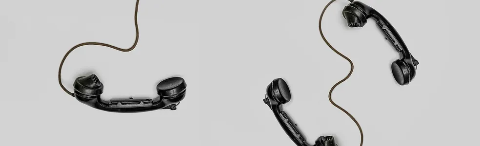 Two vintage black telephone handsets connected by cords on gray background.