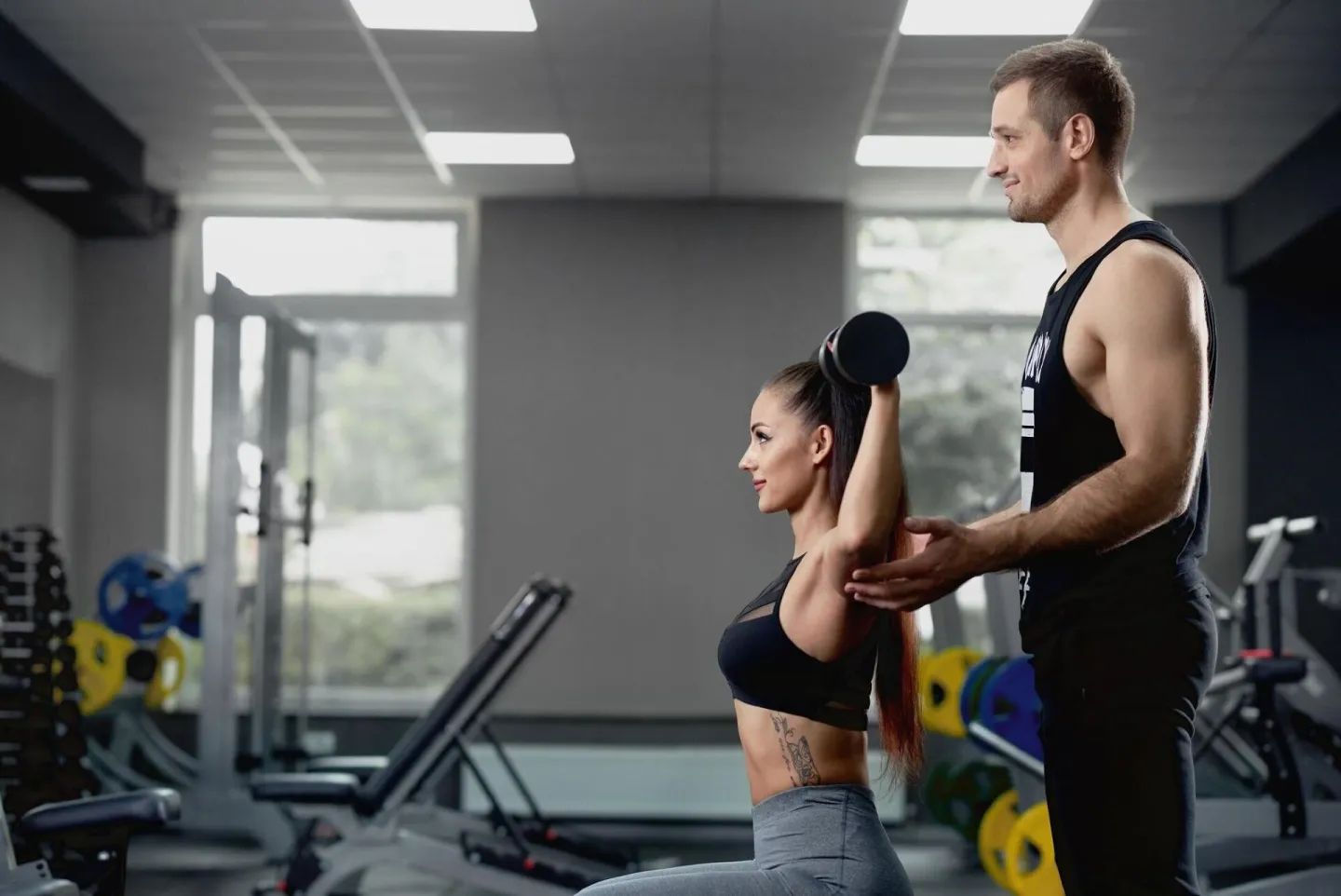 Male personal trainer helping woman working with heavy dumbb