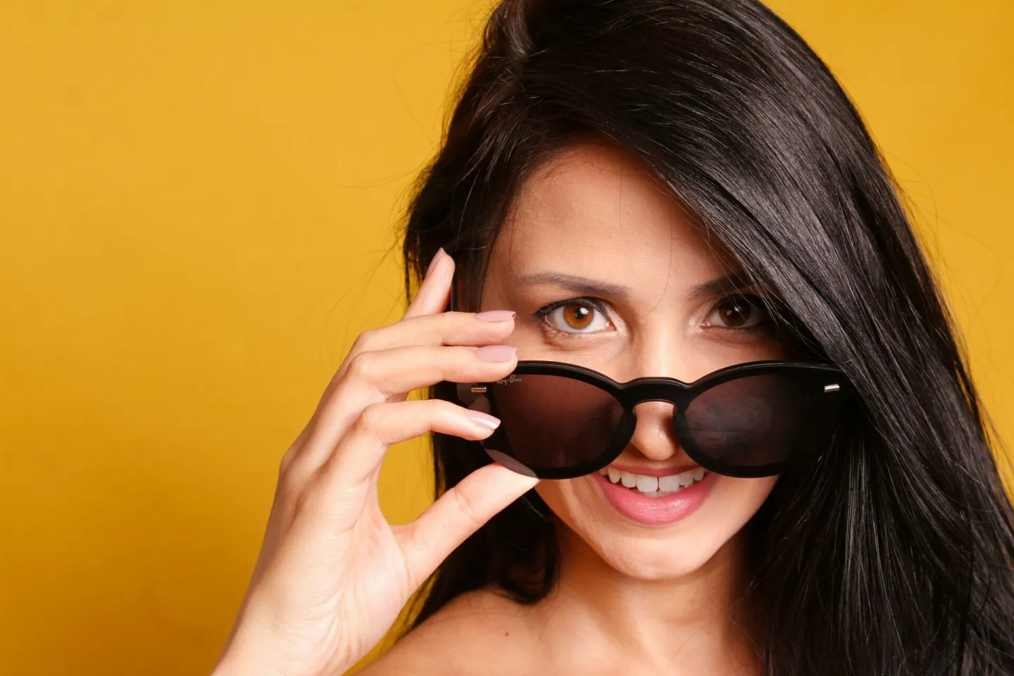 Portrait of a smiling woman with sunglasses posing against a vibrant yellow background, exuding style and confidence.