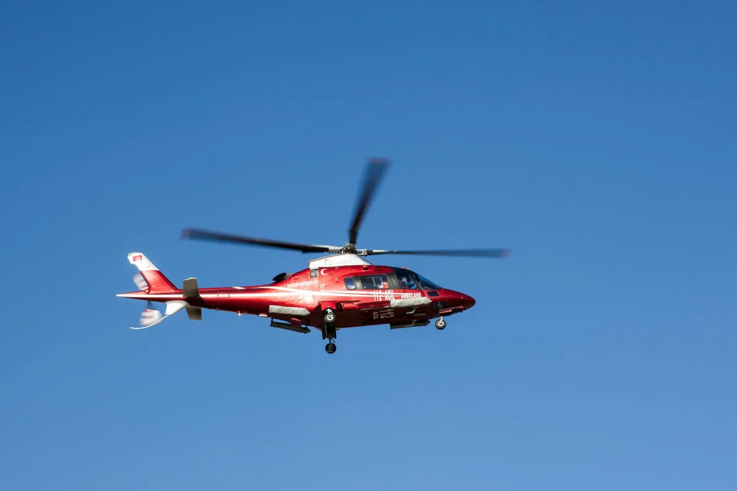 Red helicopter flying against clear blue sky, symbolizing emergency medical rescue.