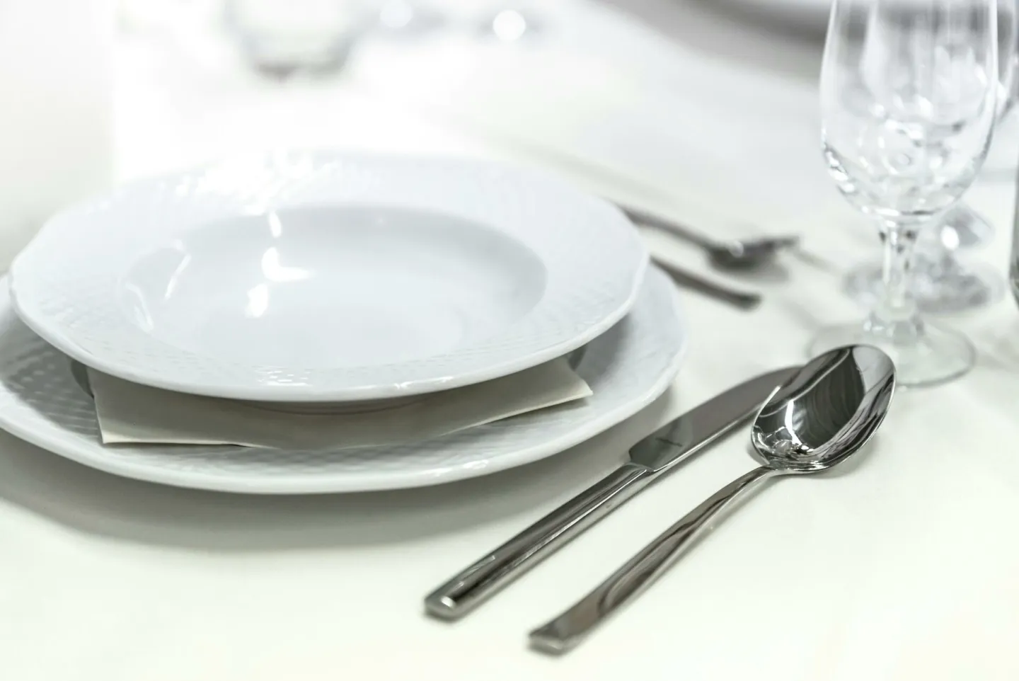 Elegant dining table with white porcelain plates and silver cutlery elegantly arranged.