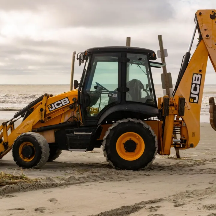A JCB backhoe parked on the sandy shores of