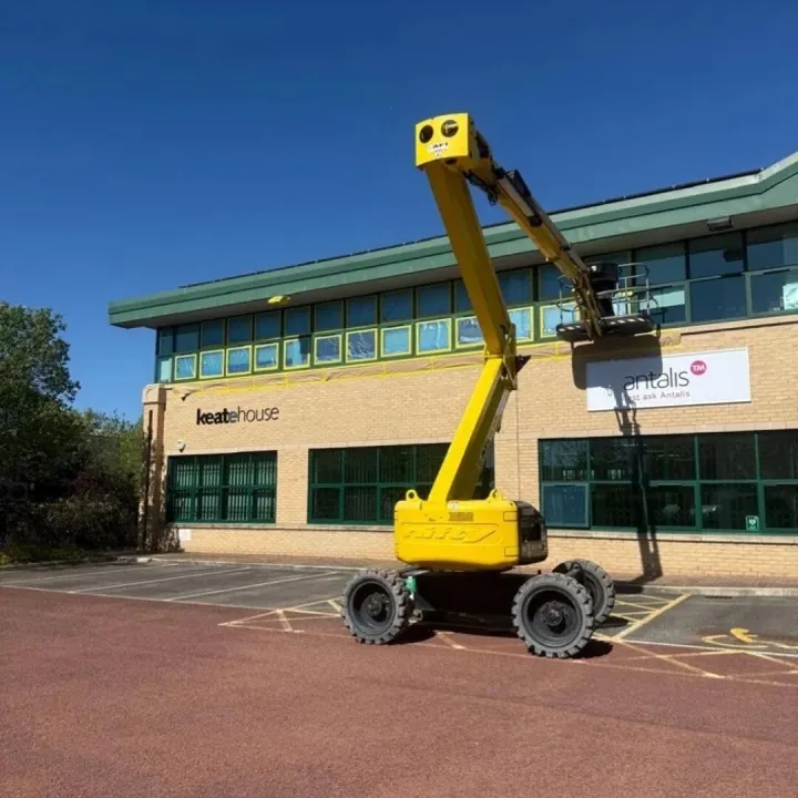 Yellow boom lift raised against a brick office building with green window frames masked for spraying