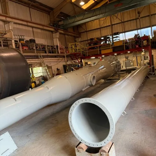 Two long topcoated grey steel chimney sections in a workshop, one showing its bolted flange end