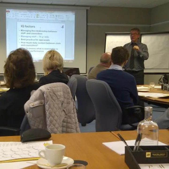 A trainer presenting a slide to delegates seated at tables during a training session