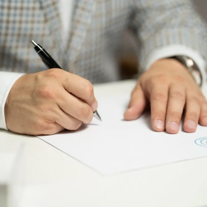 A hand signing a document with a pen