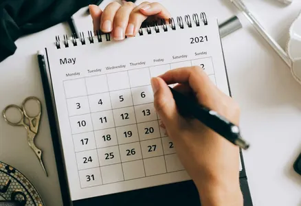 Top view of hands using a planner with coffee and accessories, focused on May 2021 calendar.