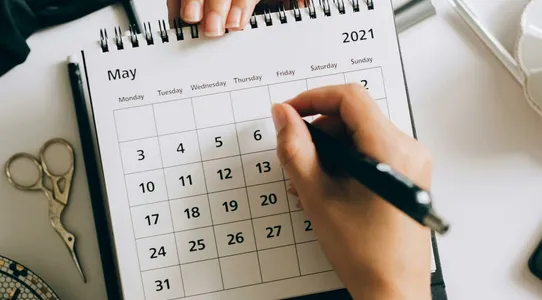 Top view of hands using a planner with coffee and accessories, focused on May 2021 calendar.