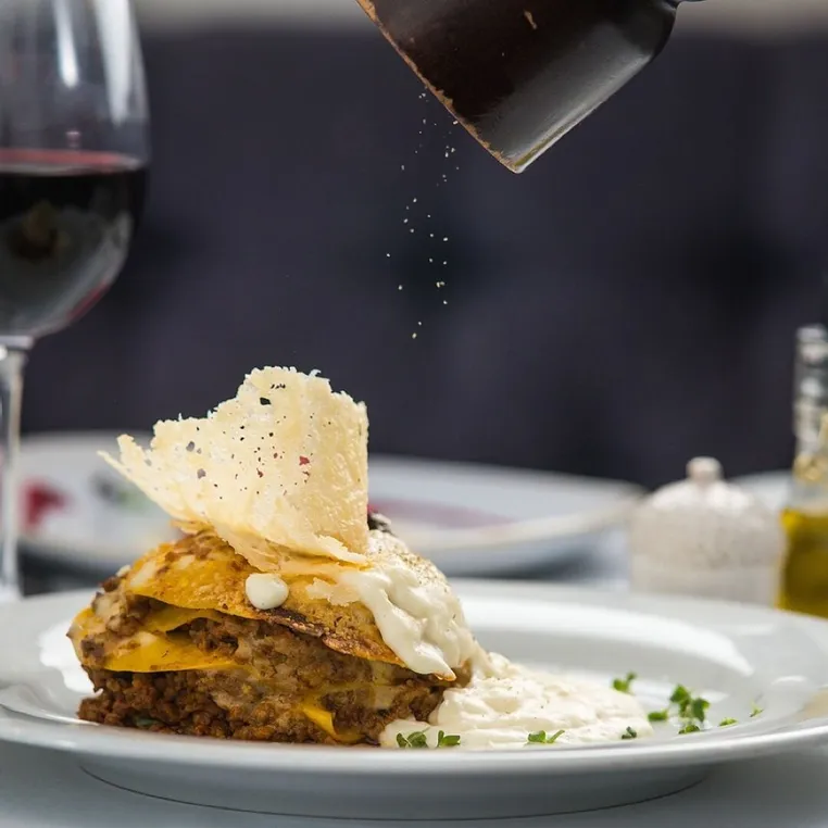 A layered pasta dish with a parmesan crisp, served with red wine