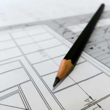 Detailed image of a black pencil resting on architectural blueprints, ideal for design and planning themes.