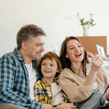 A cheerful family enjoys time together on a couch surrounded by moving boxes in their new home.