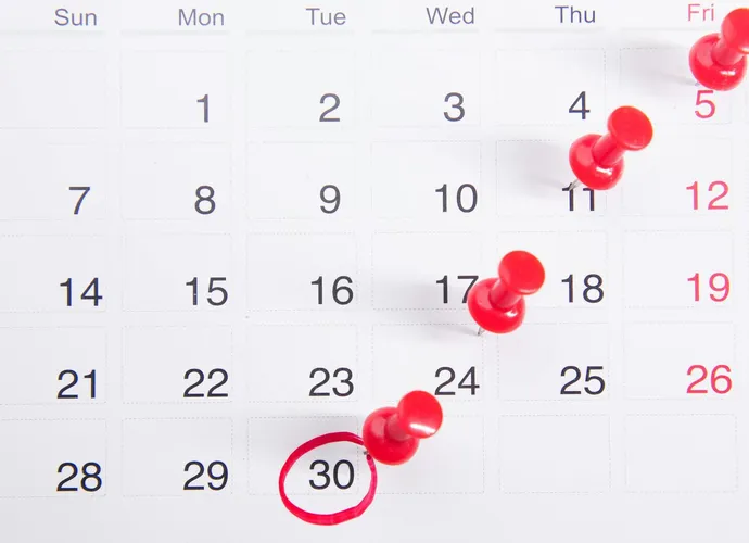 Close-up of a calendar with red push pins marking