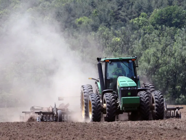 A green tractor plowing a field, creating clouds