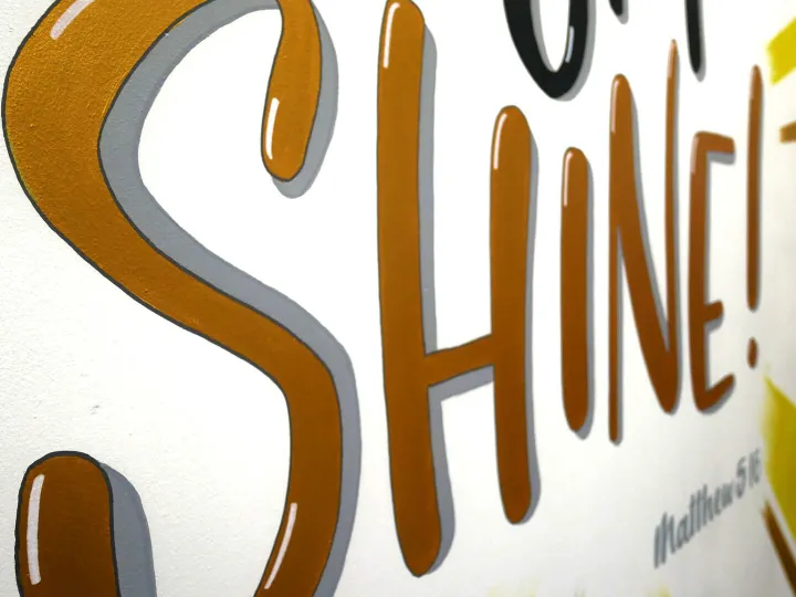 The word Shine hand lettered in gold on white board