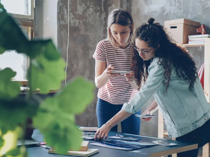 Two women looking over printed designs laid out on a table