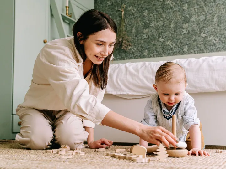 Parent sitting on the floor playing with wooden toys with a baby