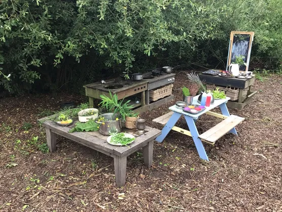 The mud kitchen, herb table and picnic bench under the trees