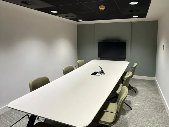 Meeting room with a long white table, green chairs, a wall-mounted screen and a muted green feature wall