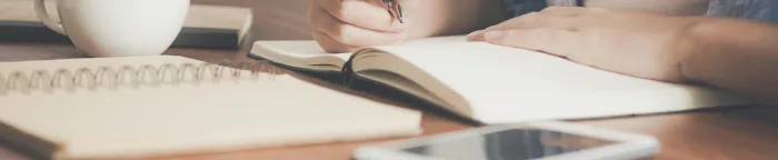 Woman Writing on a Notebook Beside Teacup and Tablet Computer