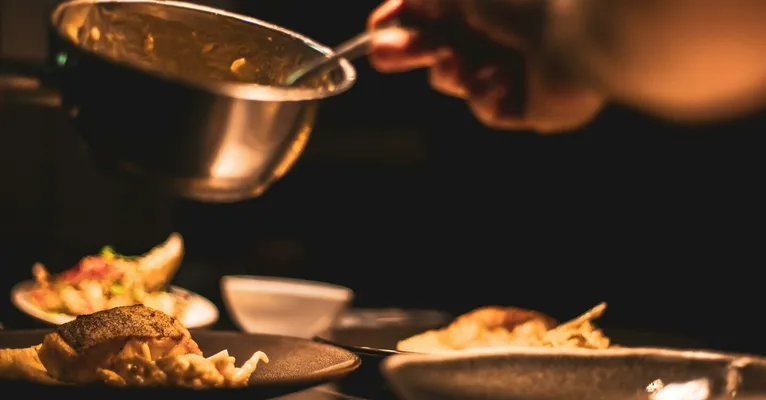Gourmet dish being plated by a chef in a dimly lit restaurant's kitchen.