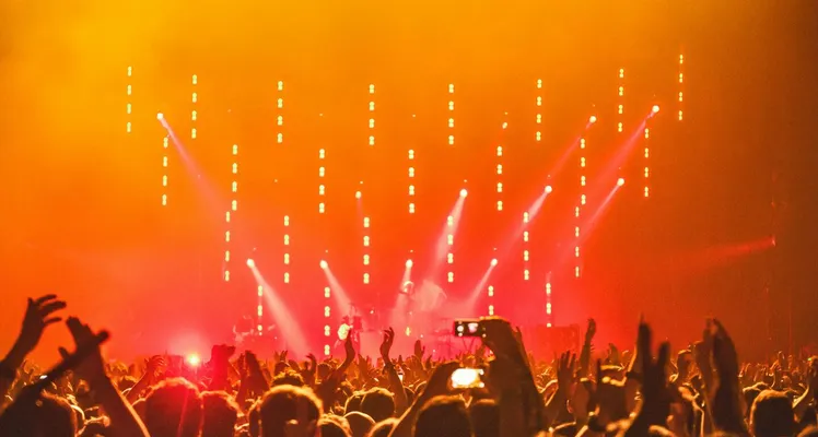 Energetic crowd at a live concert with bright stage lights and hands raised in celebration.