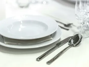 Elegant dining table with white porcelain plates and silver cutlery elegantly arranged.