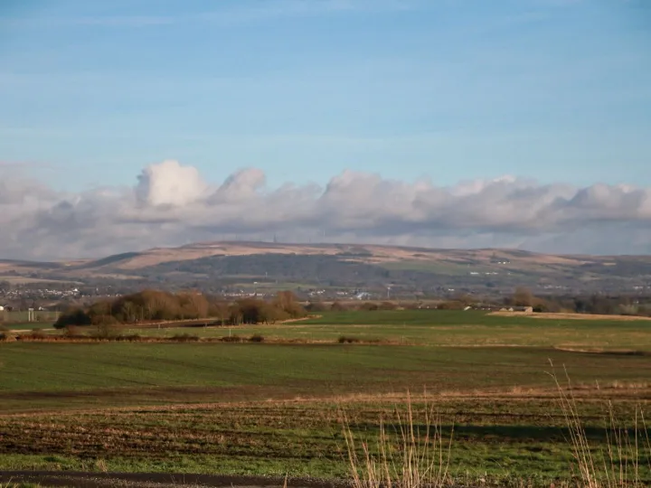 Panoramic shot of green fields and hills under a cloudy blue