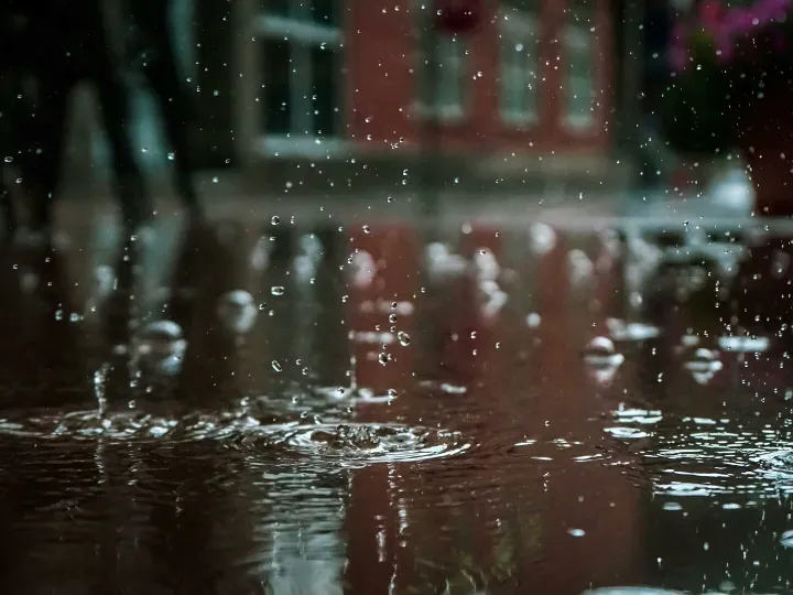 Close-up of raindrops splashing into a puddle, capturing reflections and textures in an outdoor urban setting.